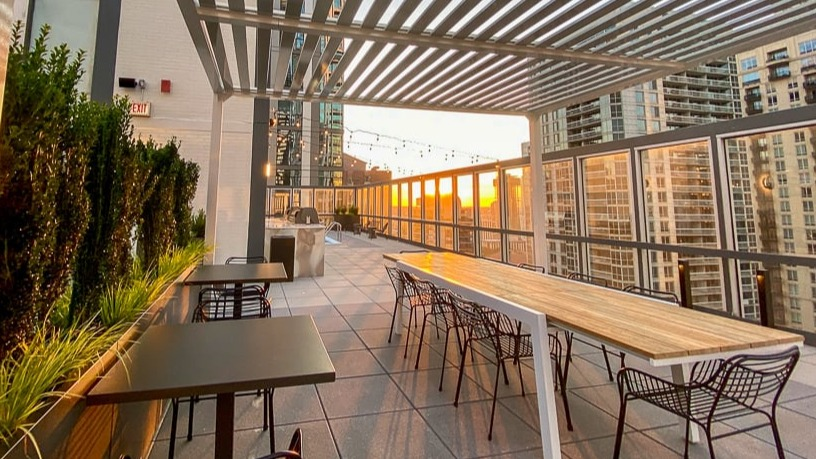 Rooftop terrace with pergola shade, communal dining tables, and skyline sunset views at 21 E Chestnut apartments in Chicago