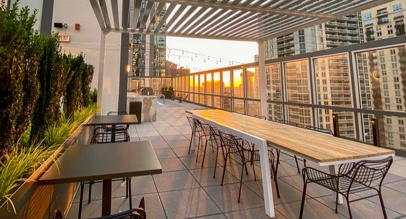 Rooftop terrace with pergola shade, communal dining tables, and skyline sunset views at 21 E Chestnut apartments in Chicago