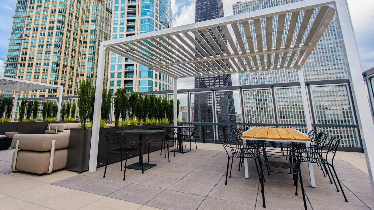 Skyline terrace with pergola shade, outdoor tables, and long communal dining area at 21 E Chestnut apartments in Chicago
