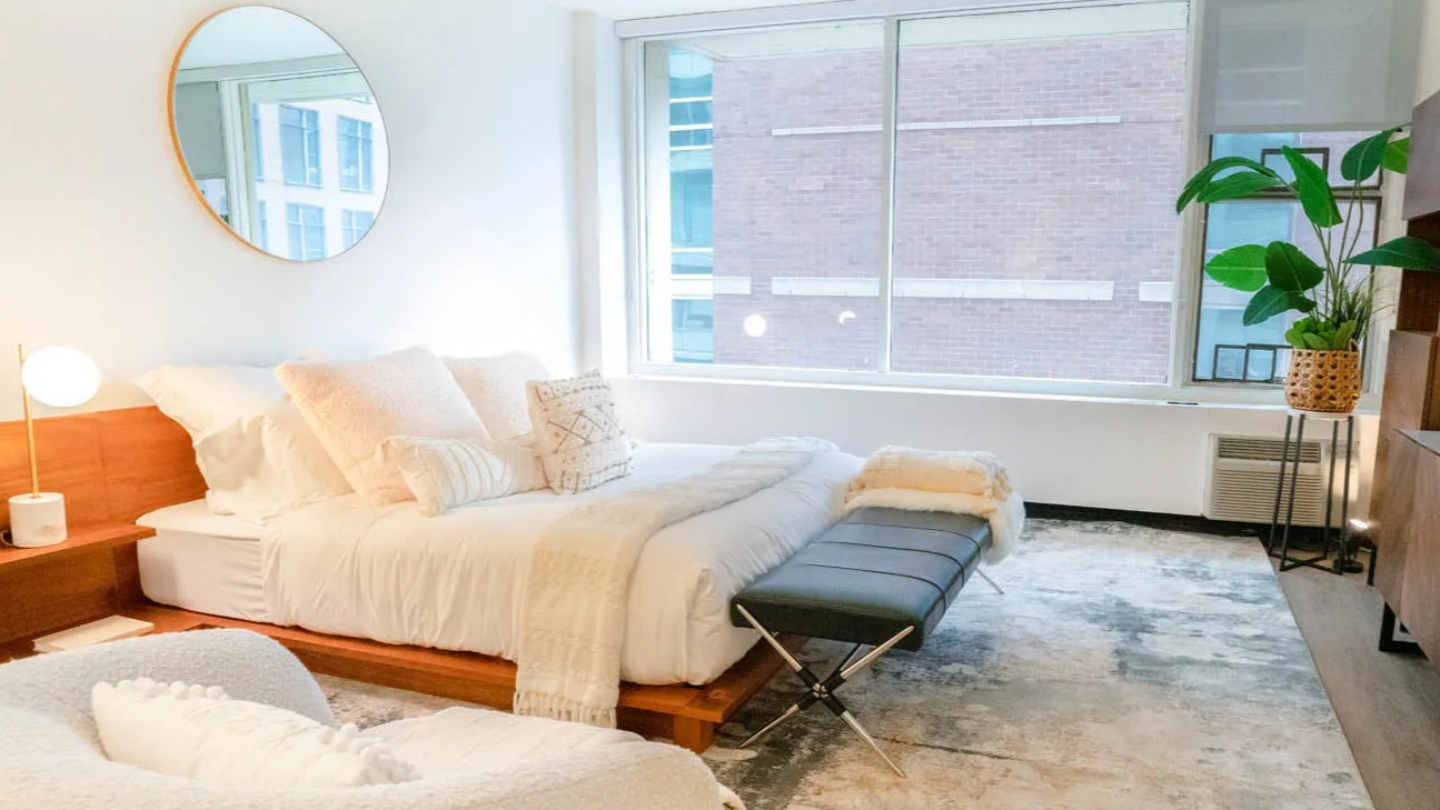 Spacious studio bedroom with large window, wood platform bed, bench seating, abstract rug, and media console at 21 E Chestnut in Chicago