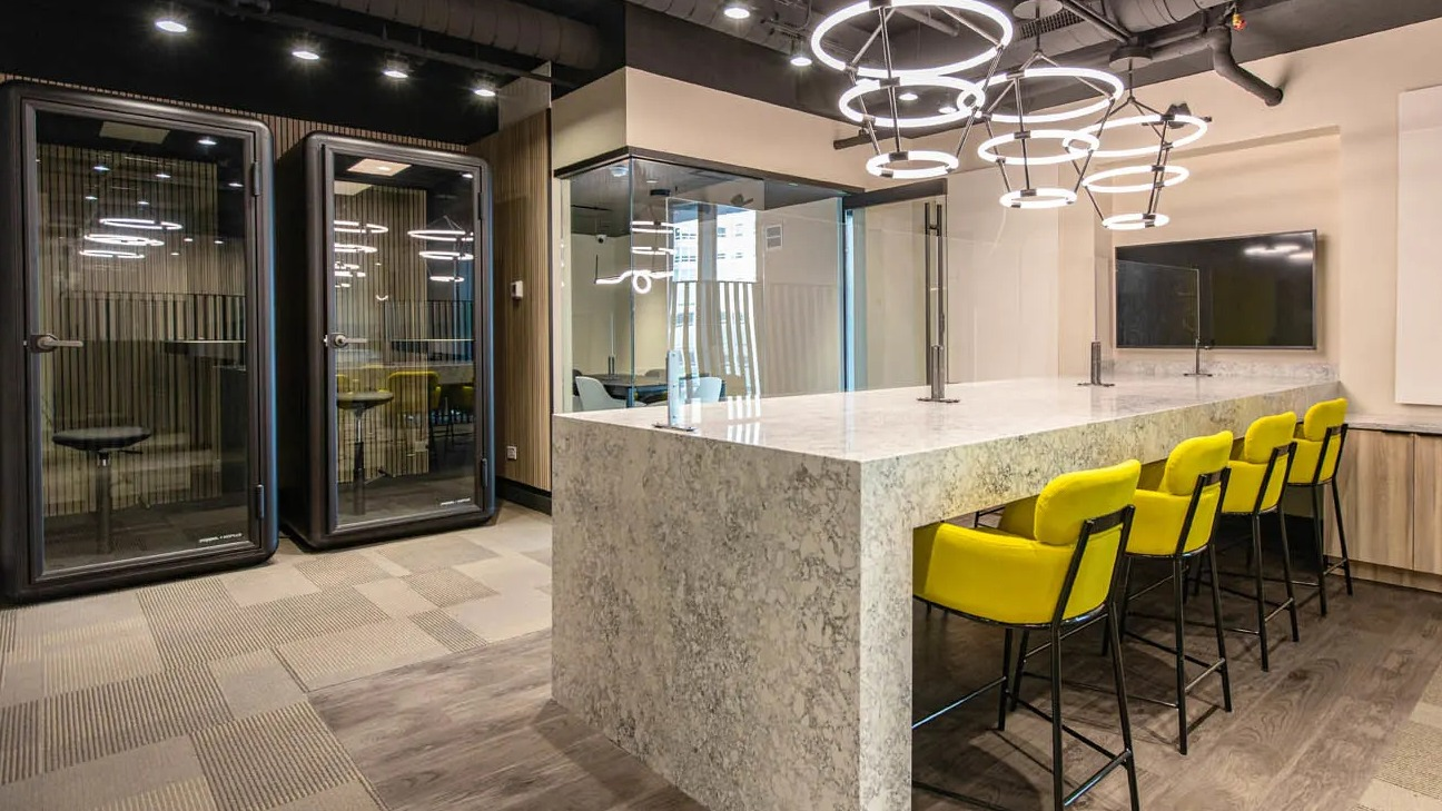 Work lounge and coworking space with phone booths, ring pendant lights, and a long stone island at 21 E Chestnut apartments in Chicago