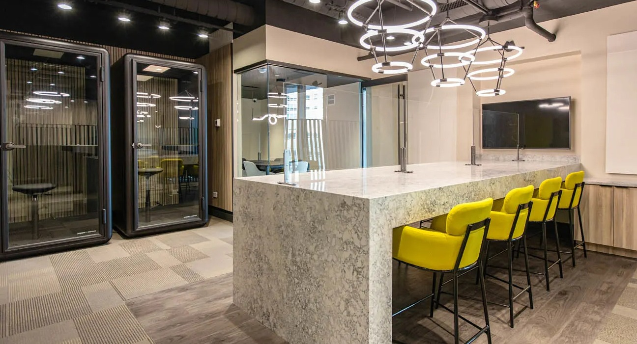 Work lounge and coworking space with phone booths, ring pendant lights, and a long stone island at 21 E Chestnut apartments in Chicago