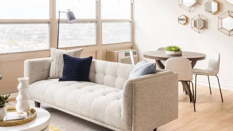 Bright living and dining area with a tufted sofa, round table, and geometric wall mirrors at 2101 South Michigan Apartments in Chicago, offering great natural light