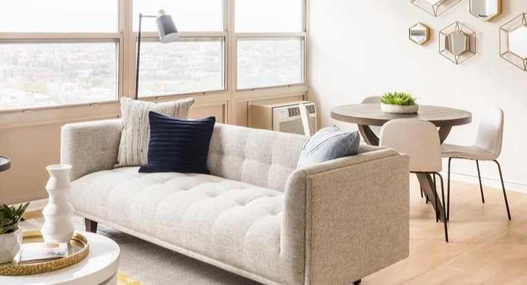 Bright living and dining area with a tufted sofa, round table, and geometric wall mirrors at 2101 South Michigan Apartments in Chicago, offering great natural light