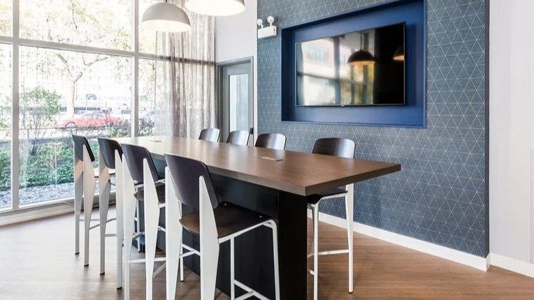 Coworking space with a high-top table, pendant lighting, and a wall-mounted TV beside floor-to-ceiling windows at 2101 South Michigan Apartments in Chicago