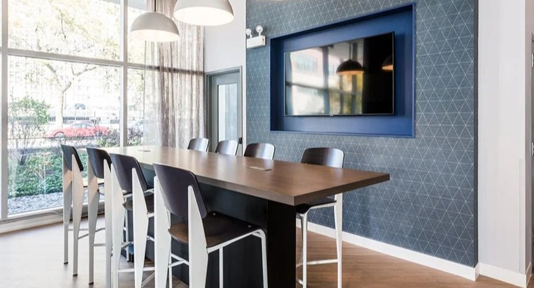 Coworking space with a high-top table, pendant lighting, and a wall-mounted TV beside floor-to-ceiling windows at 2101 South Michigan Apartments in Chicago