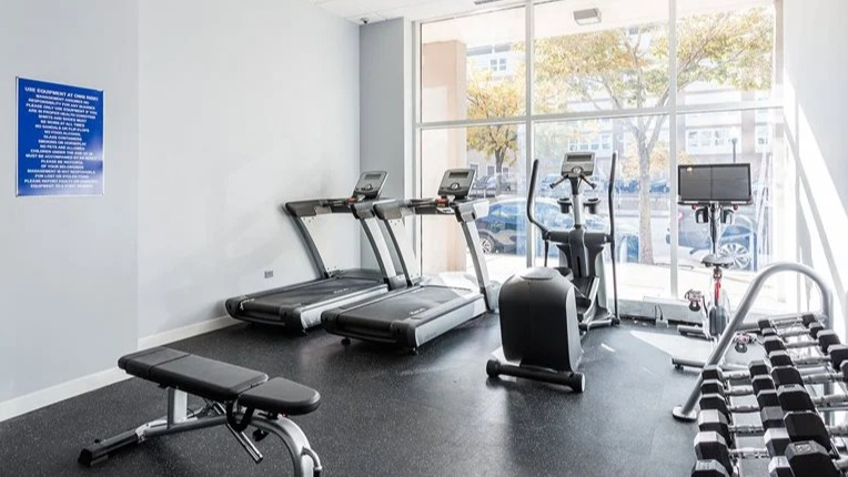 Light-filled fitness center with treadmills, a stationary bike, free weights, and a bench at 2101 South Michigan Apartments in Chicago, perfect for daily cardio sessions