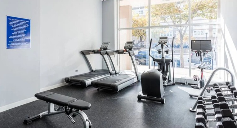 Light-filled fitness center with treadmills, a stationary bike, free weights, and a bench at 2101 South Michigan Apartments in Chicago, perfect for daily cardio sessions