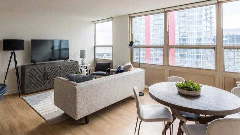 Spacious living room with large windows, skyline views, TV console, and comfortable seating at 2101 South Michigan Apartments in Chicago, designed for relaxed entertaining