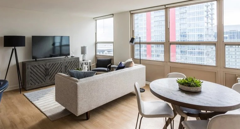 Spacious living room with large windows, skyline views, TV console, and comfortable seating at 2101 South Michigan Apartments in Chicago, designed for relaxed entertaining
