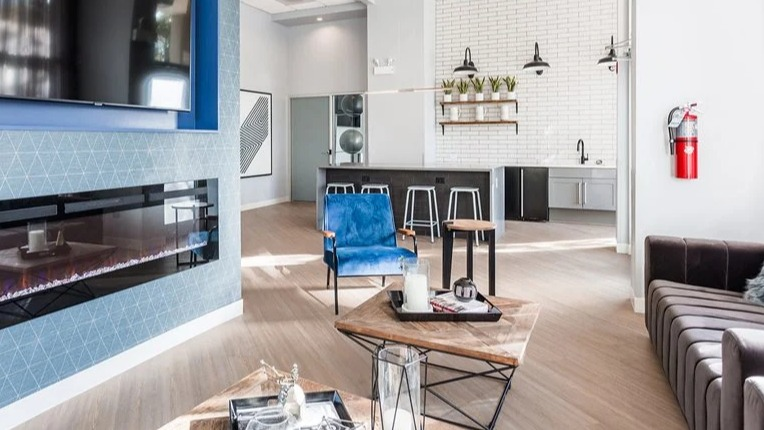 Resident lounge with linear fireplace and TV, blue accent chair, and an open community kitchen with stools at 2101 South Michigan Apartments in Chicago.