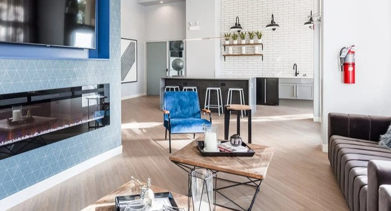 Resident lounge with linear fireplace and TV, blue accent chair, and an open community kitchen with stools at 2101 South Michigan Apartments in Chicago.