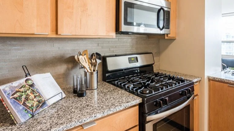 Modern kitchen with stainless-steel gas range and microwave, granite countertops, and warm wood cabinets at 2101 South Michigan Apartments in Chicago, ready for home cooking