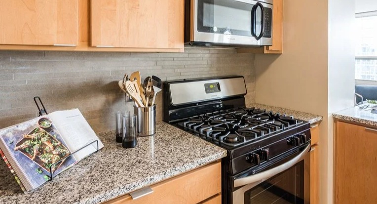 Modern kitchen with stainless-steel gas range and microwave, granite countertops, and warm wood cabinets at 2101 South Michigan Apartments in Chicago, ready for home cooking