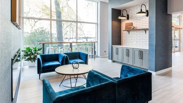 Modern lobby seating area with blue armchairs, a round table, and a built-in coffee station under subway tiles at 2101 South Michigan Apartments in Chicago