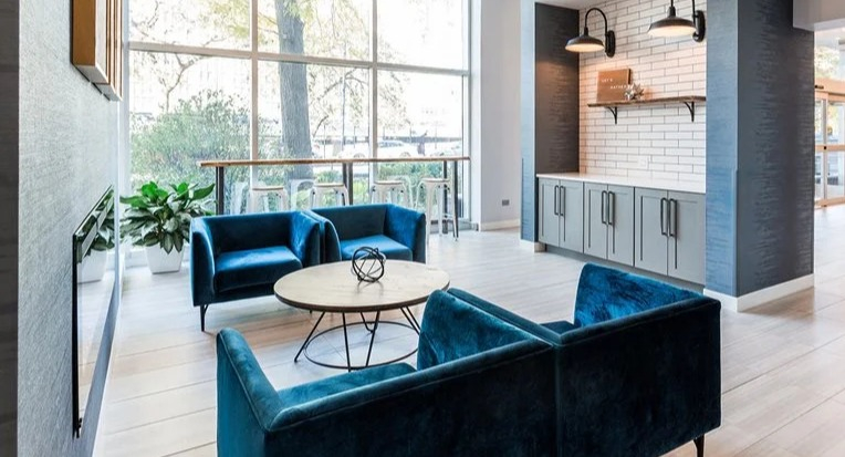 Modern lobby seating area with blue armchairs, a round table, and a built-in coffee station under subway tiles at 2101 South Michigan Apartments in Chicago