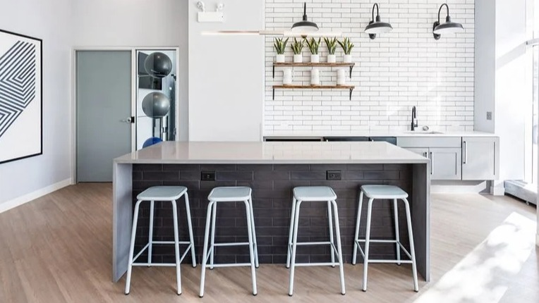 Resident social kitchen with a large island, bar stools, and a white subway tile backsplash under industrial lights at 2101 South Michigan Apartments in Chicago