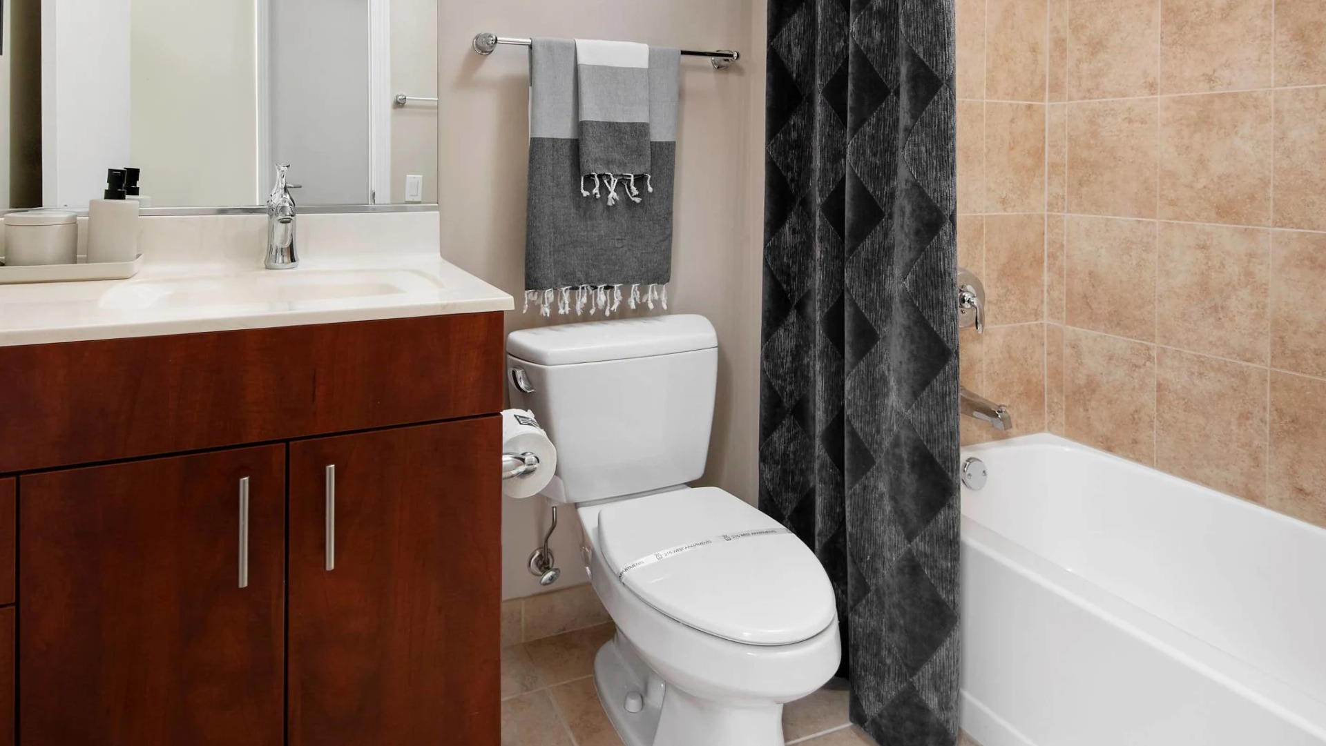 Modern bathroom at 215 West apartments in Chicago featuring a wide vanity, framed mirror, toilet, and tub-shower with tan tile and dark curtain