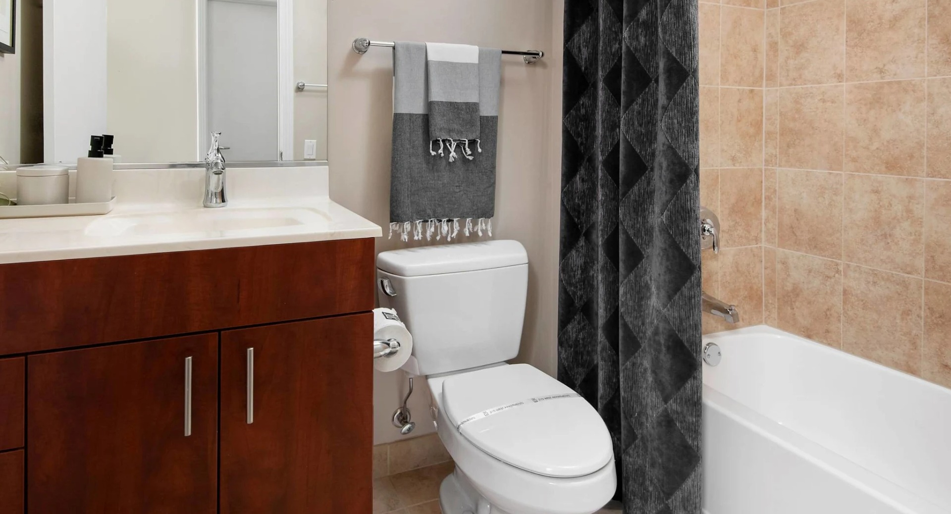 Modern bathroom at 215 West apartments in Chicago featuring a wide vanity, framed mirror, toilet, and tub-shower with tan tile and dark curtain