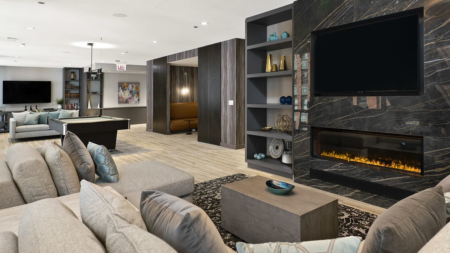Upscale club lounge at 215 West Chicago featuring modern sofas, built-in shelves, a linear fireplace, and a large TV for relaxing