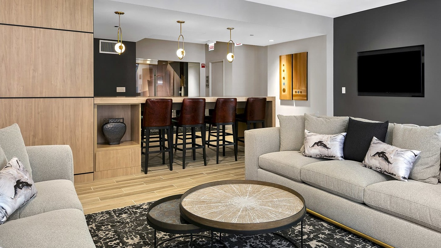 Elegant clubroom at 215 West with plush sofas, nesting coffee tables, and a long bar with leather stools, ideal for gatherings and watch parties
