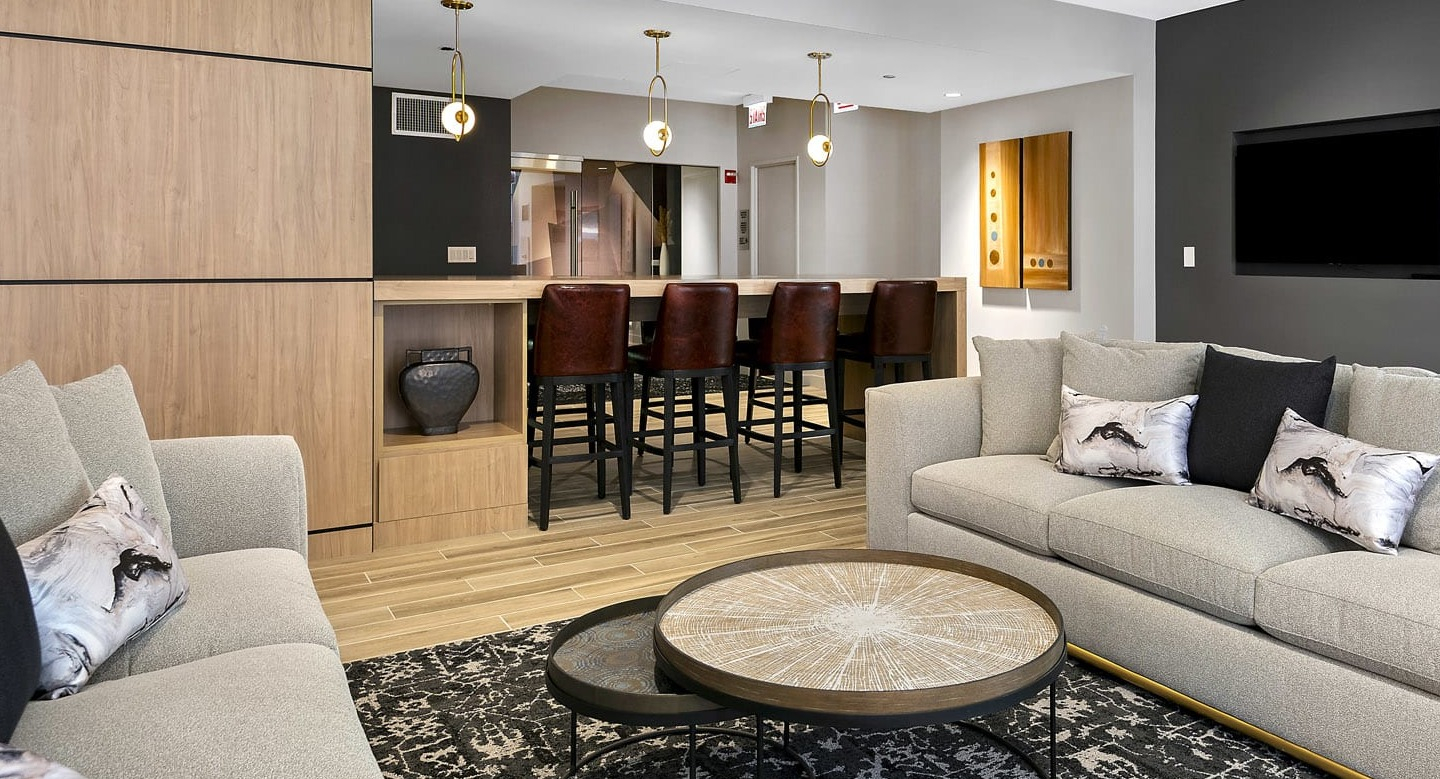 Elegant clubroom at 215 West with plush sofas, nesting coffee tables, and a long bar with leather stools, ideal for gatherings and watch parties