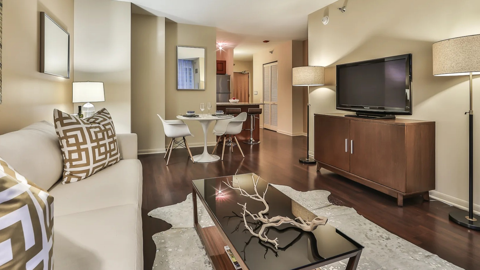 Cozy living and dining area at 215 West apartments, with a sofa, TV console, round table, and hardwood floors leading toward the kitchen and entry hall