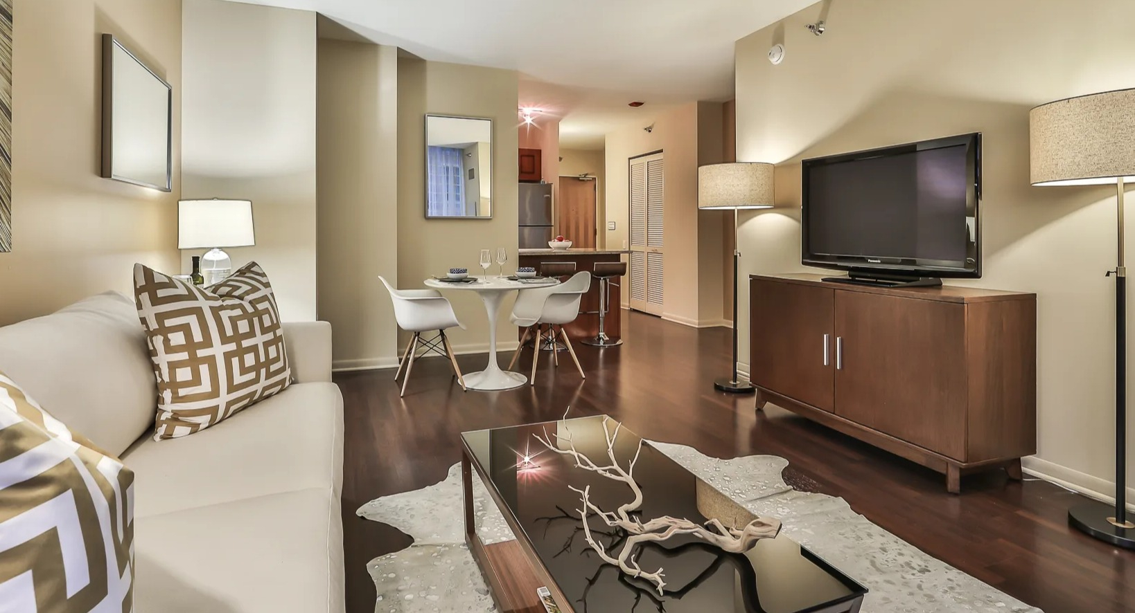 Cozy living and dining area at 215 West apartments, with a sofa, TV console, round table, and hardwood floors leading toward the kitchen and entry hall