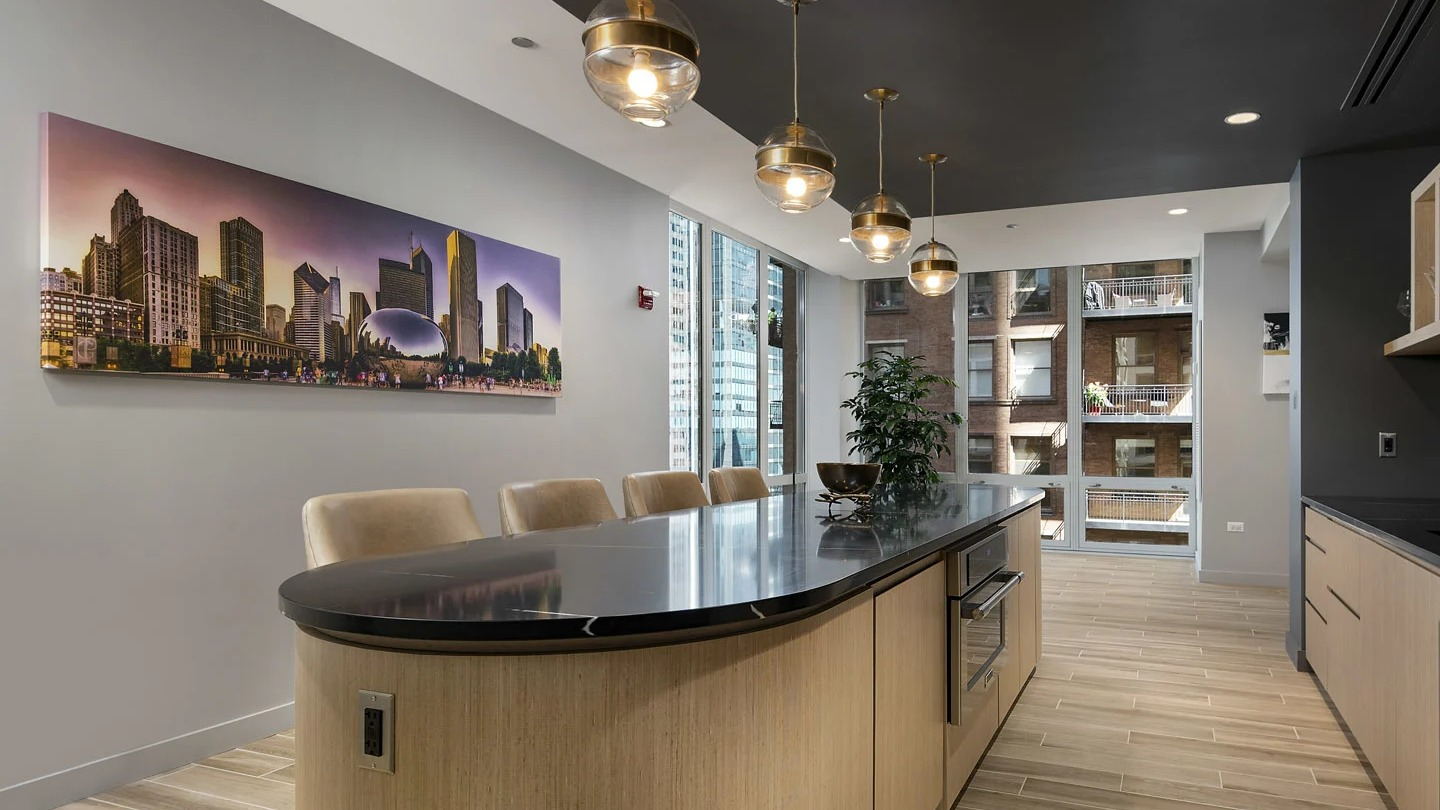 Modern kitchen lounge at 215 West Chicago with an expansive island, black countertops, glassware shelving, and statement globe pendant lights