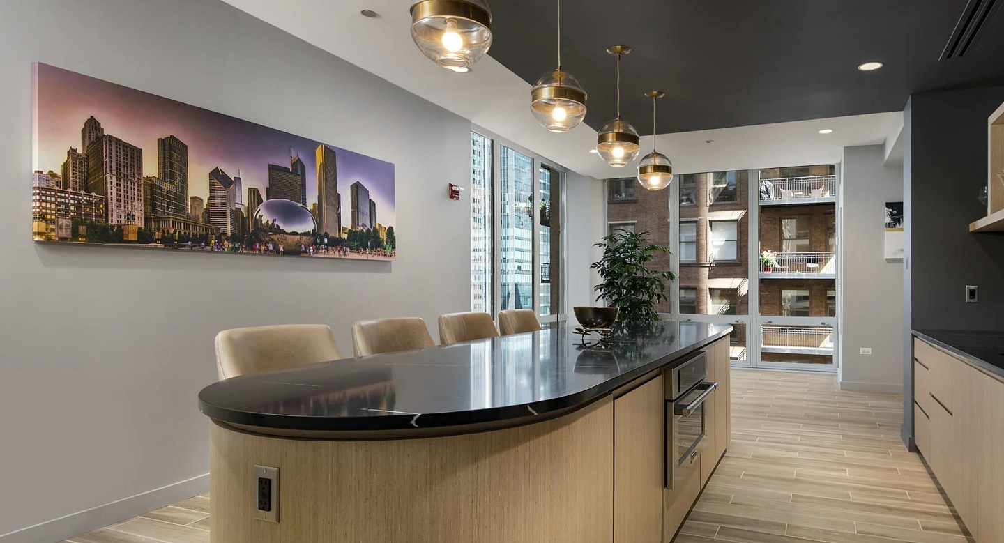 Modern kitchen lounge at 215 West Chicago with an expansive island, black countertops, glassware shelving, and statement globe pendant lights