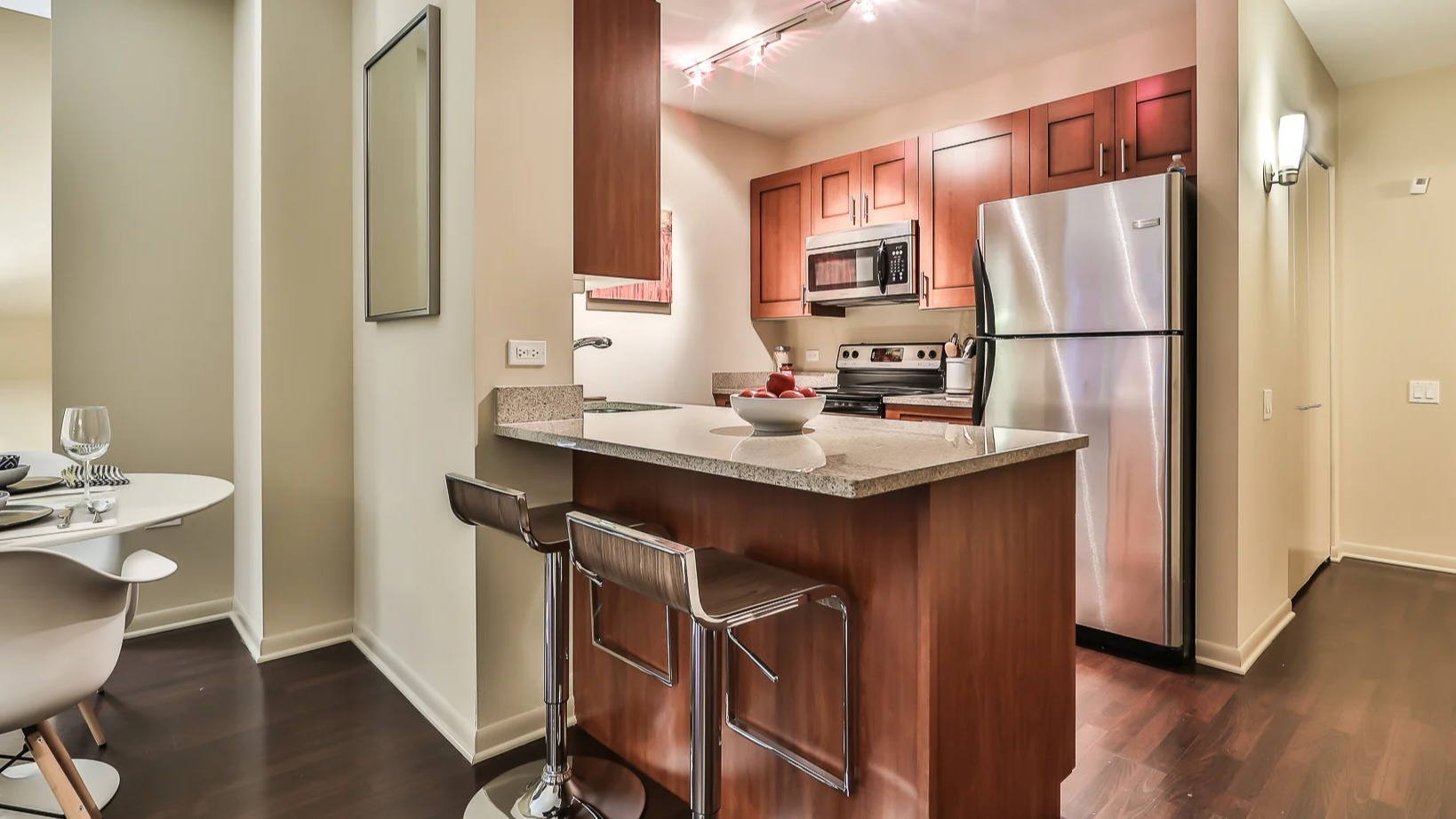 Modern kitchen at 215 West in Chicago with a breakfast island and stools, stainless fridge and range, and warm wood cabinets in an efficient layout