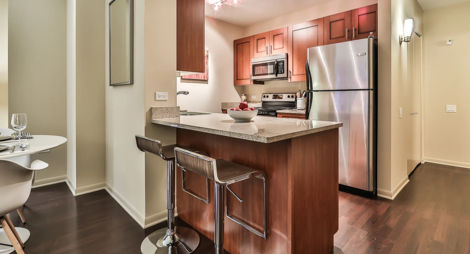 Modern kitchen at 215 West in Chicago with a breakfast island and stools, stainless fridge and range, and warm wood cabinets in an efficient layout
