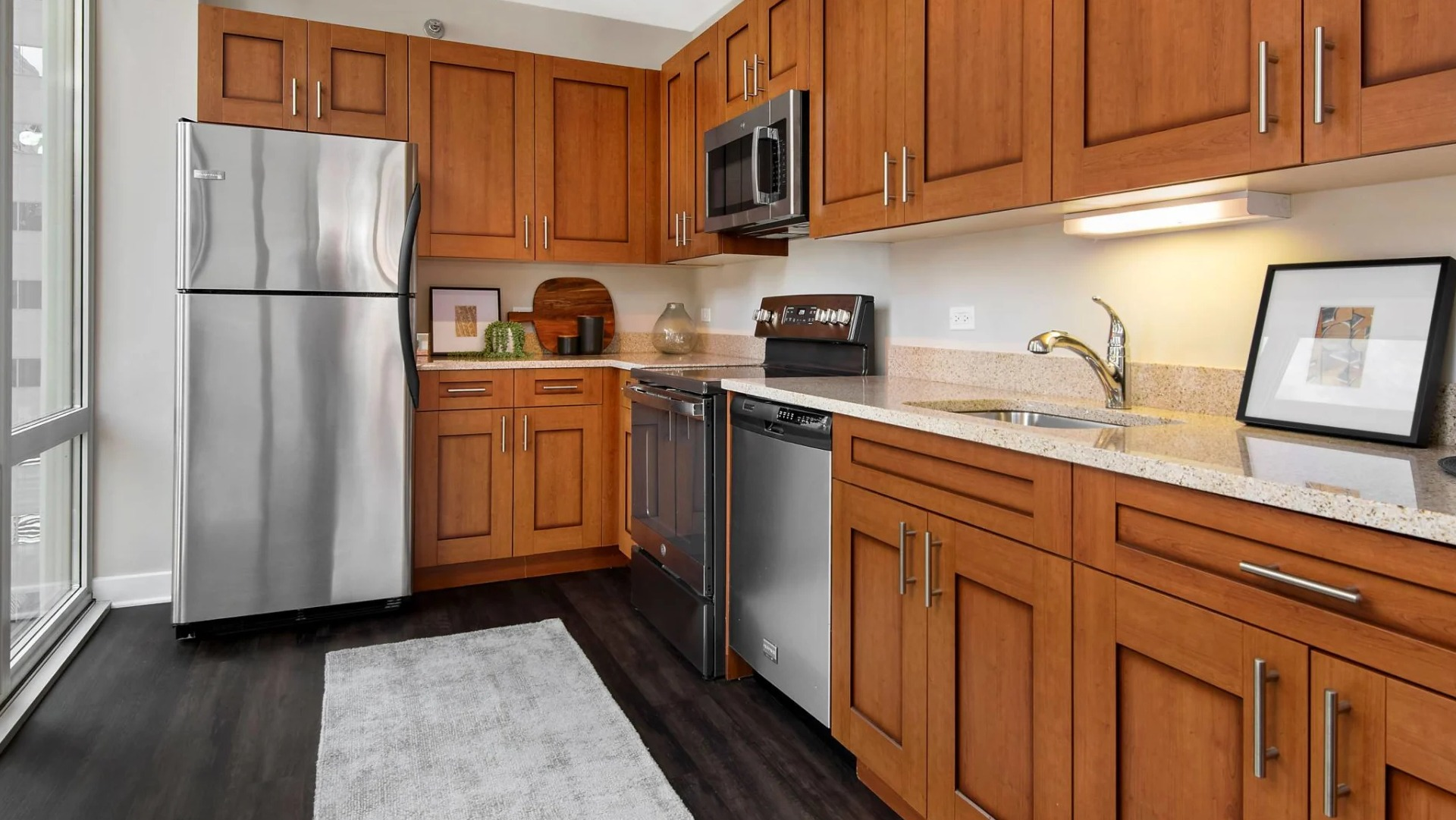 Galley kitchen at 215 West Chicago with stainless appliances, abundant wood cabinetry, stone counters, and a tall window bringing in downtown views and light