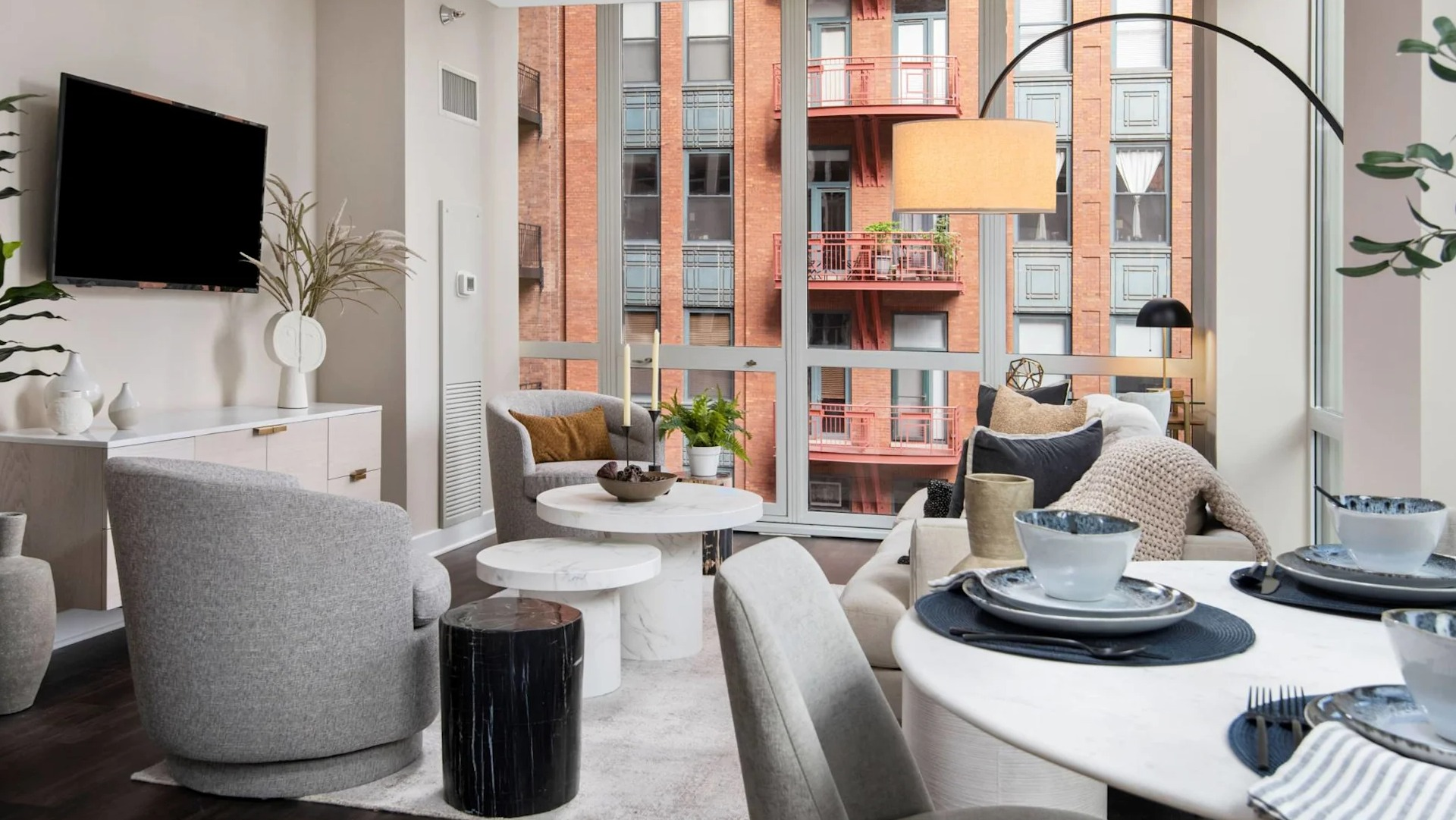 Bright living room with adjacent dining nook at 215 West in Chicago, featuring modern seating, round table settings, and panoramic windows to the city