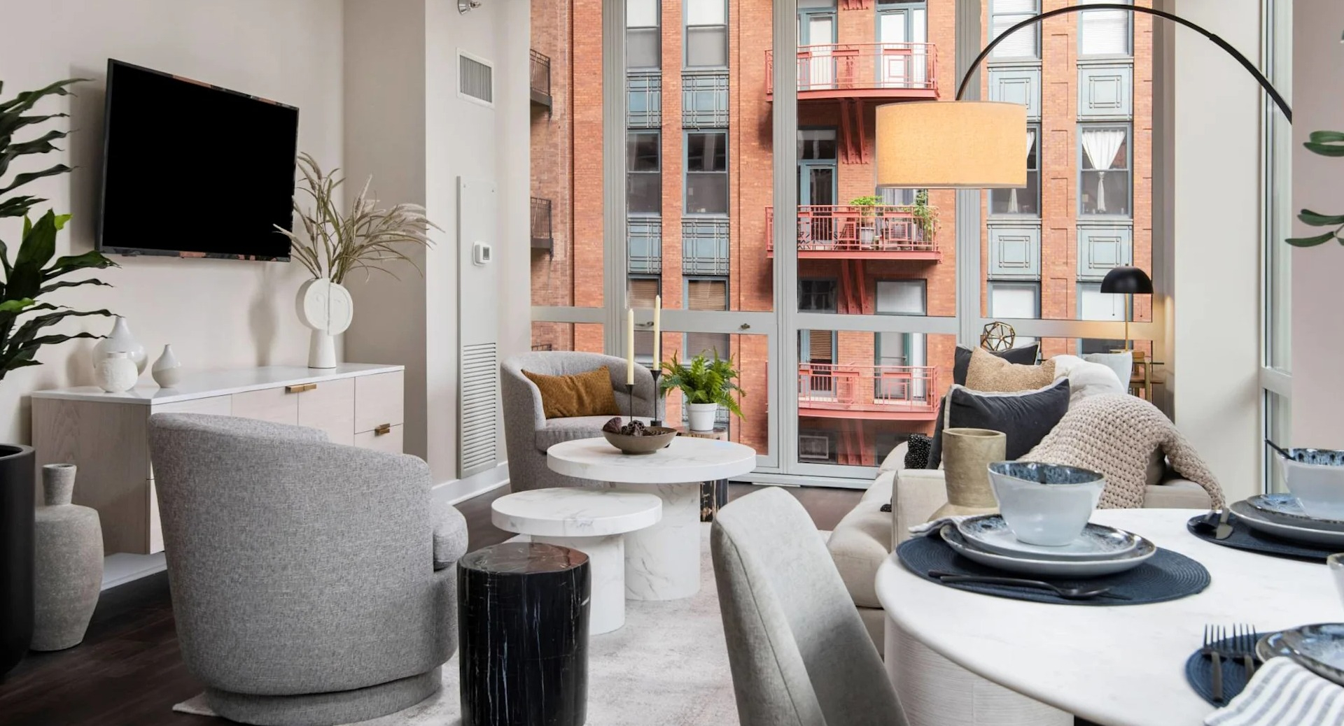 Bright living room with adjacent dining nook at 215 West in Chicago, featuring modern seating, round table settings, and panoramic windows to the city