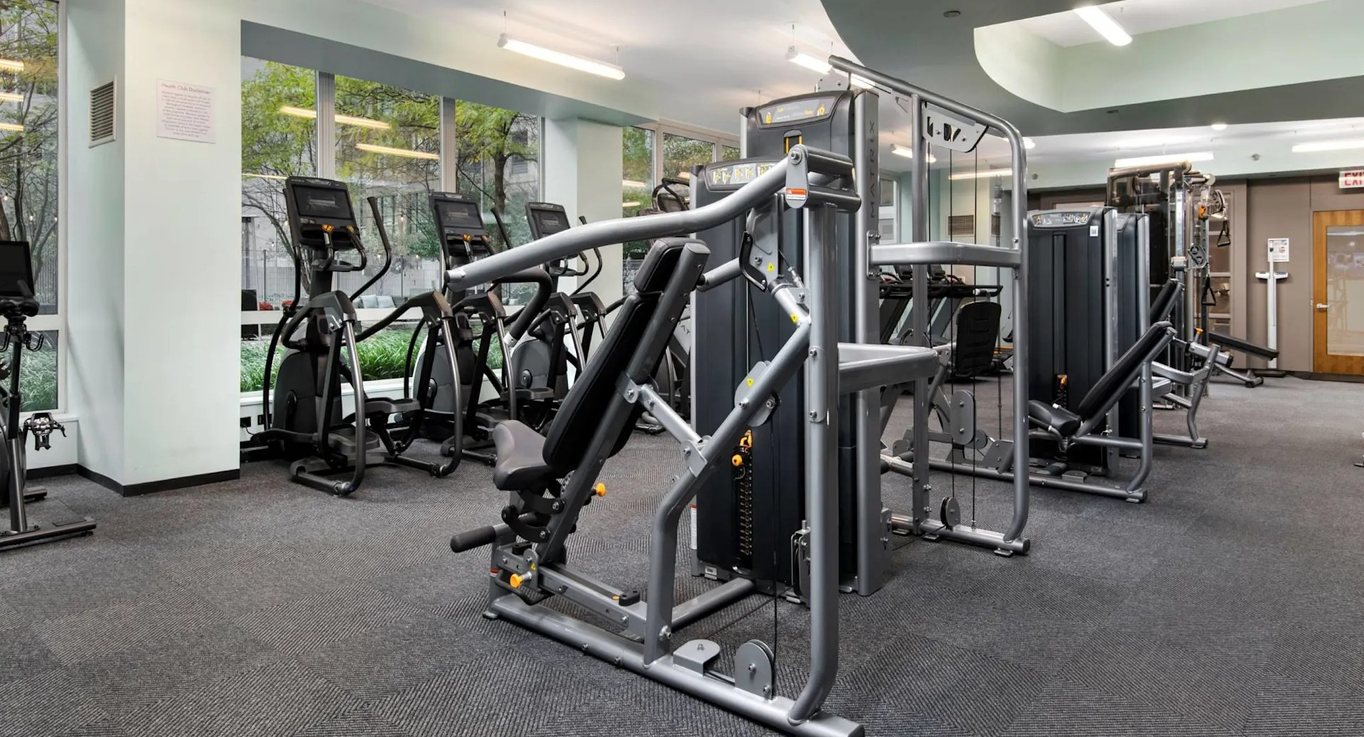 Resident fitness center at 215 West apartments in Chicago with strength machines, cardio equipment, and large windows overlooking landscaped grounds