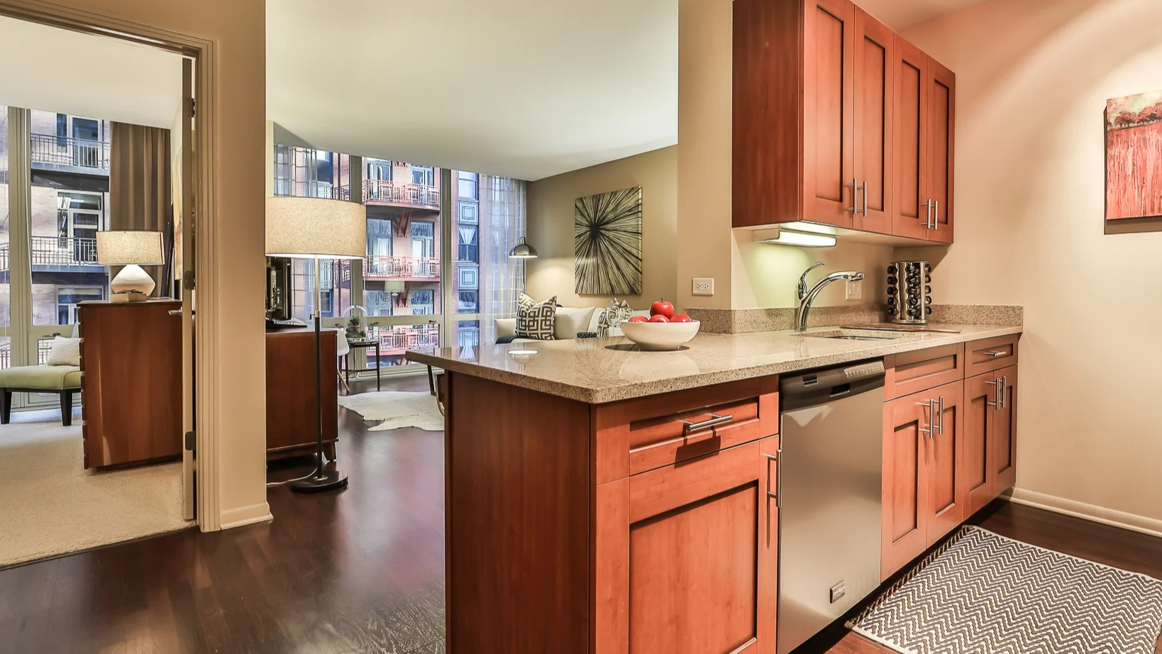 Open-concept kitchen at 215 West apartments in Chicago with wood cabinetry, granite peninsula, and a view into the bright living room with large windows