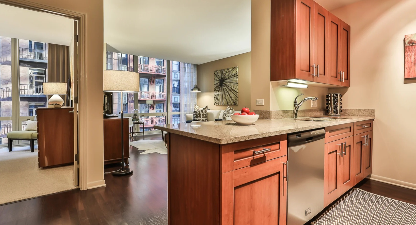 Open-concept kitchen at 215 West apartments in Chicago with wood cabinetry, granite peninsula, and a view into the bright living room with large windows