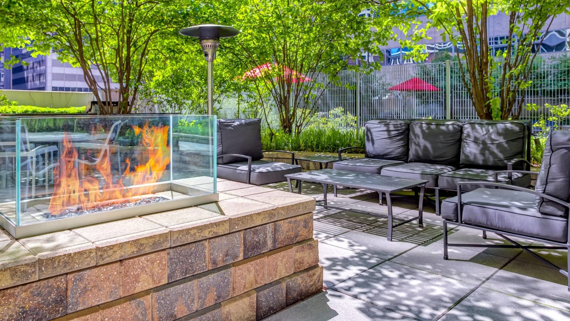 Outdoor lounge at 215 West apartments in Chicago featuring a glass-framed fire pit, cushioned seating, patio tables, and leafy landscaping for relaxing