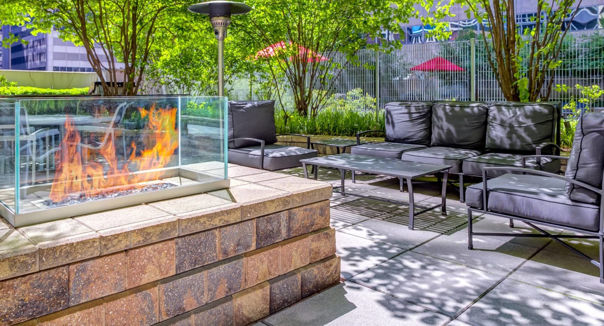 Outdoor lounge at 215 West apartments in Chicago featuring a glass-framed fire pit, cushioned seating, patio tables, and leafy landscaping for relaxing