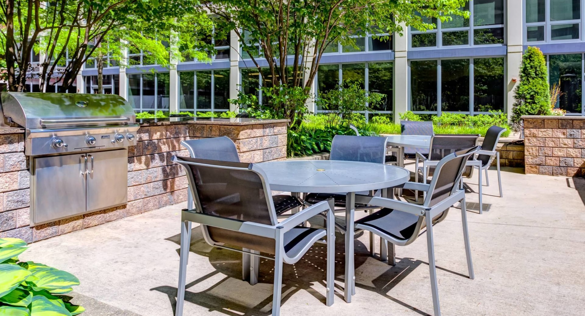 Resident grilling patio at 215 West in Chicago with stainless BBQs, café tables and chairs, and leafy landscaping in a sunny courtyard setting