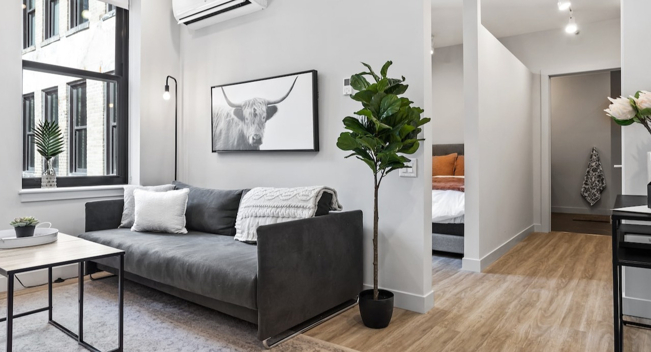 Bright living room at 330 S Wells Apartments in Chicago featuring a gray sofa, modern décor, large window, and natural light
