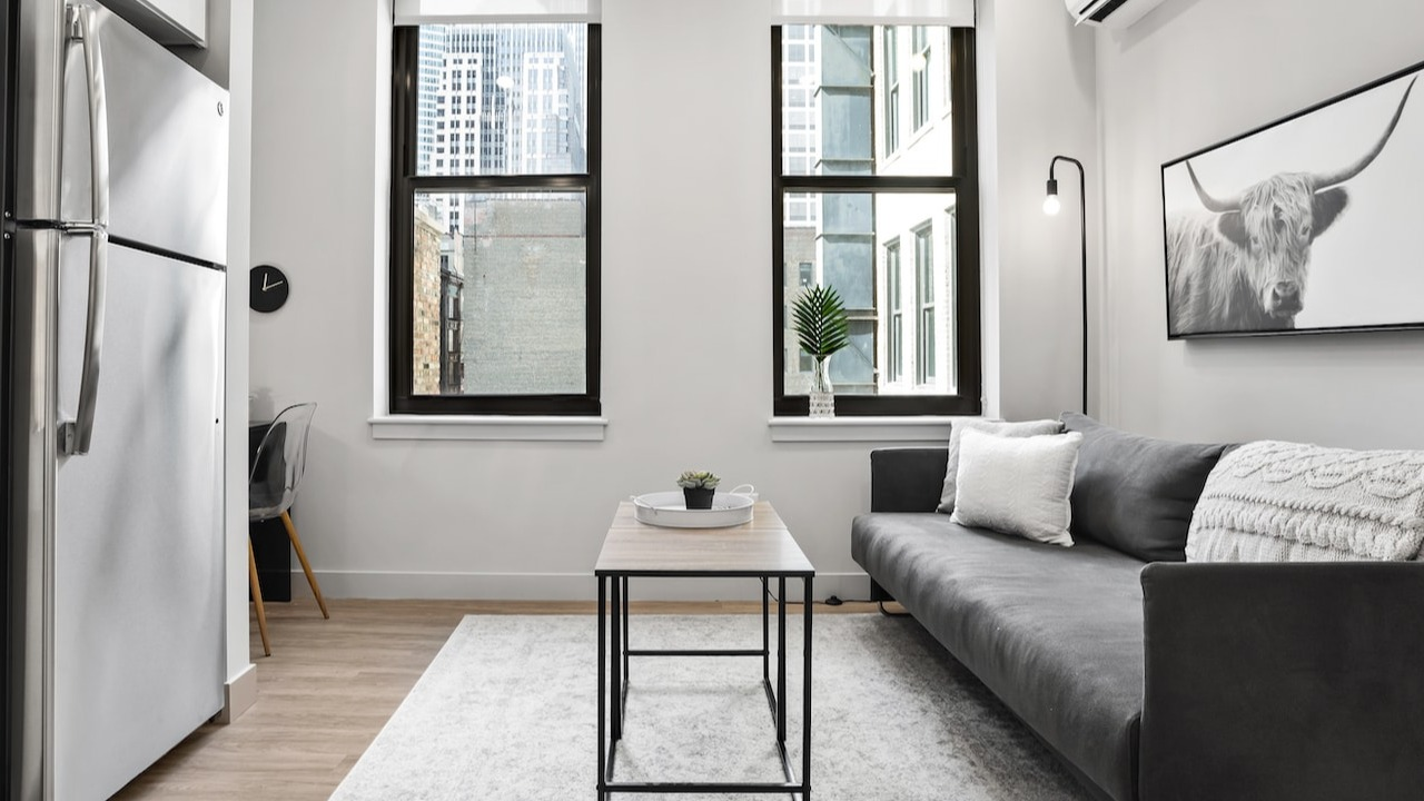 Stylish living room at 330 S Wells Apartments in Chicago with a gray sofa, wall art, and large windows for natural light