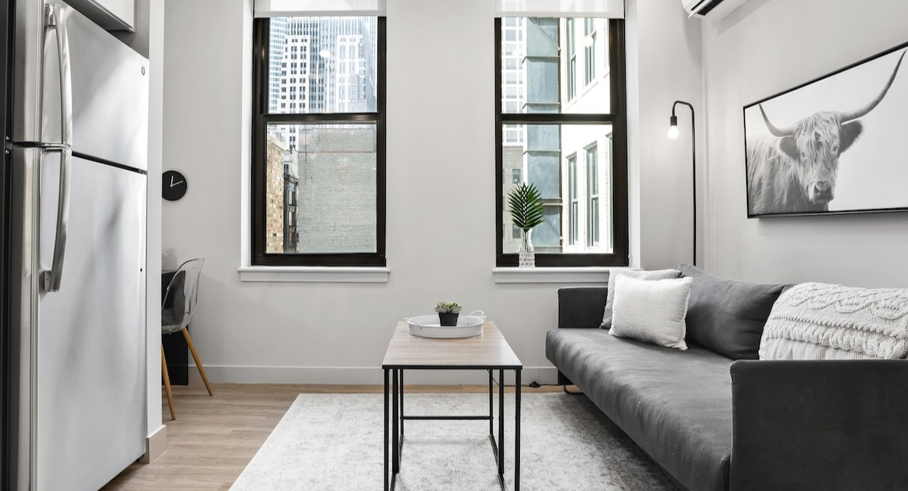 Stylish living room at 330 S Wells Apartments in Chicago with a gray sofa, wall art, and large windows for natural light