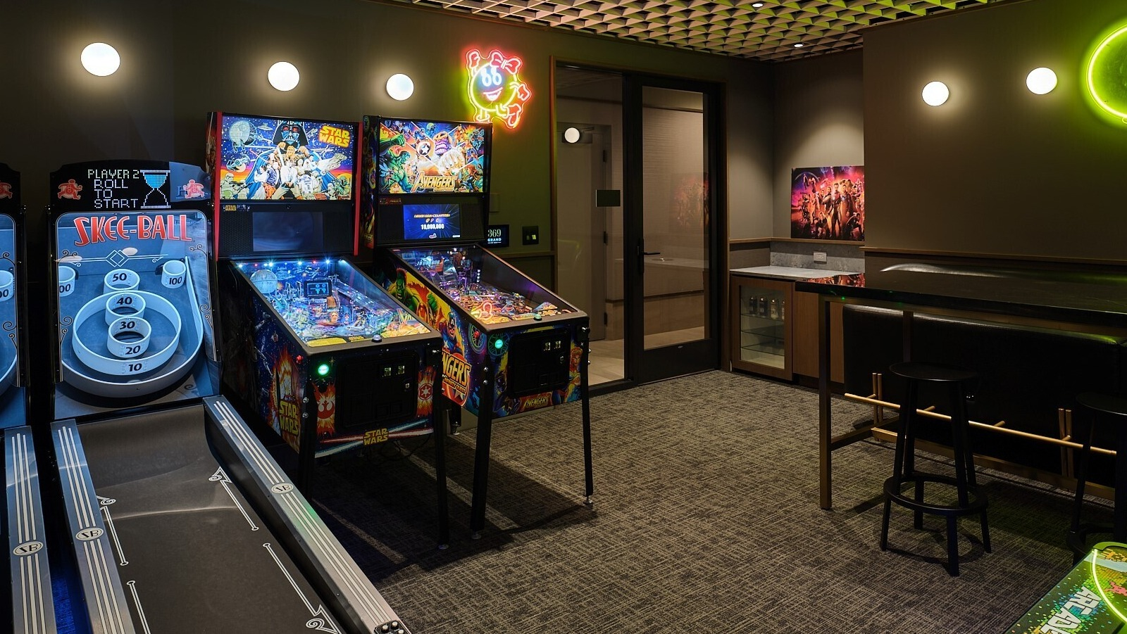 Arcade game room featuring skee-ball lanes, pinball machines, neon Pac-Man art, and bar seating at 369 Grand apartments in Chicago