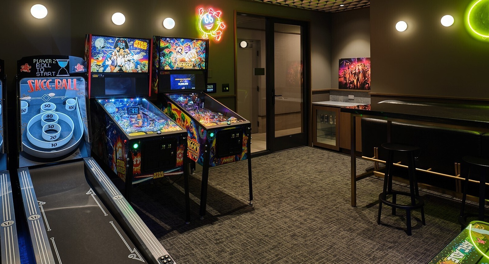 Arcade game room featuring skee-ball lanes, pinball machines, neon Pac-Man art, and bar seating at 369 Grand apartments in Chicago