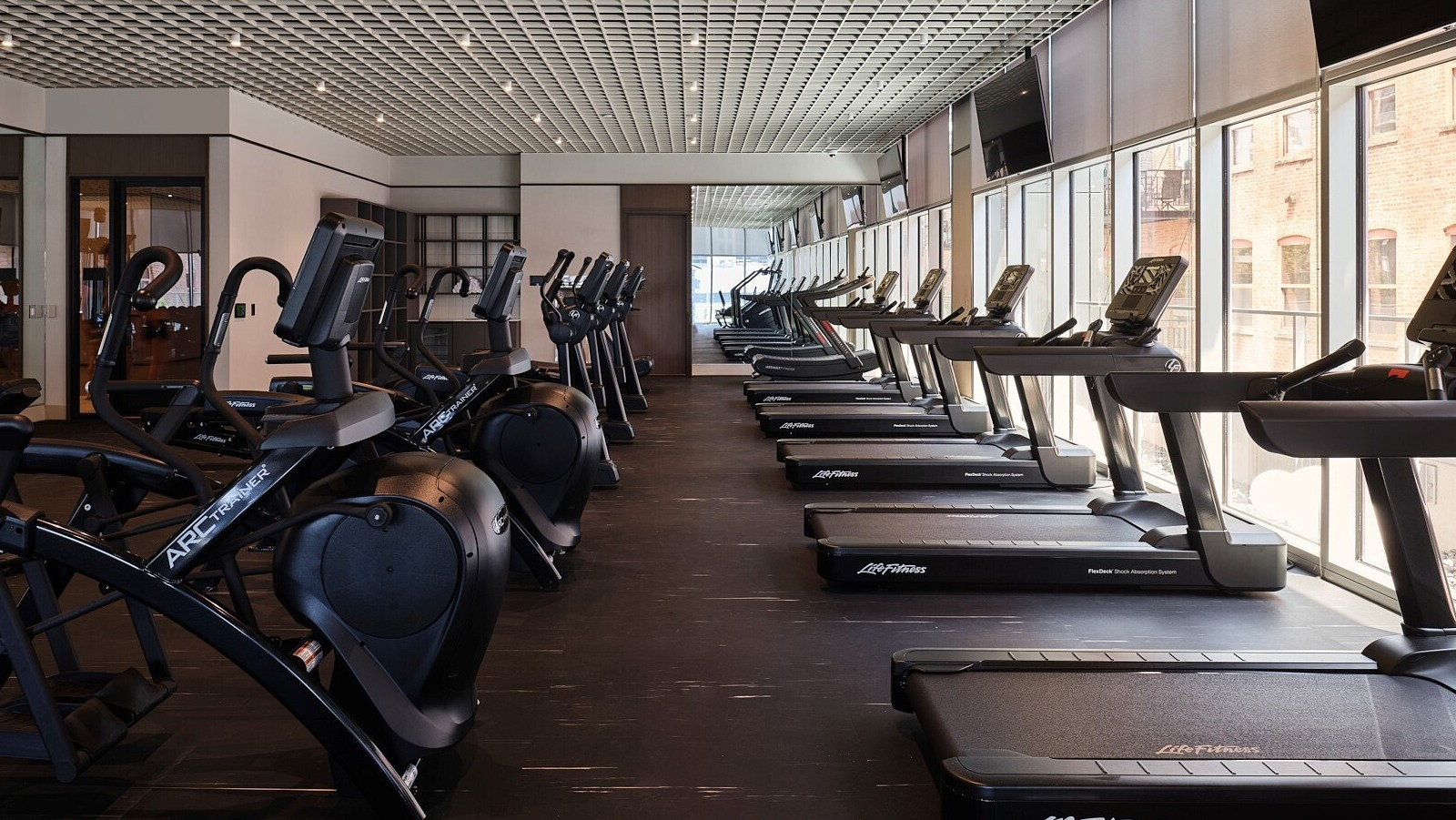 Cardio studio with a long row of treadmills facing floor-to-ceiling windows for city views at 369 Grand apartments in Chicago