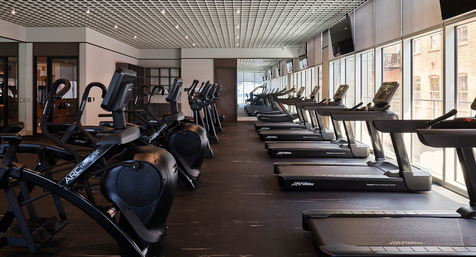Cardio studio with a long row of treadmills facing floor-to-ceiling windows for city views at 369 Grand apartments in Chicago