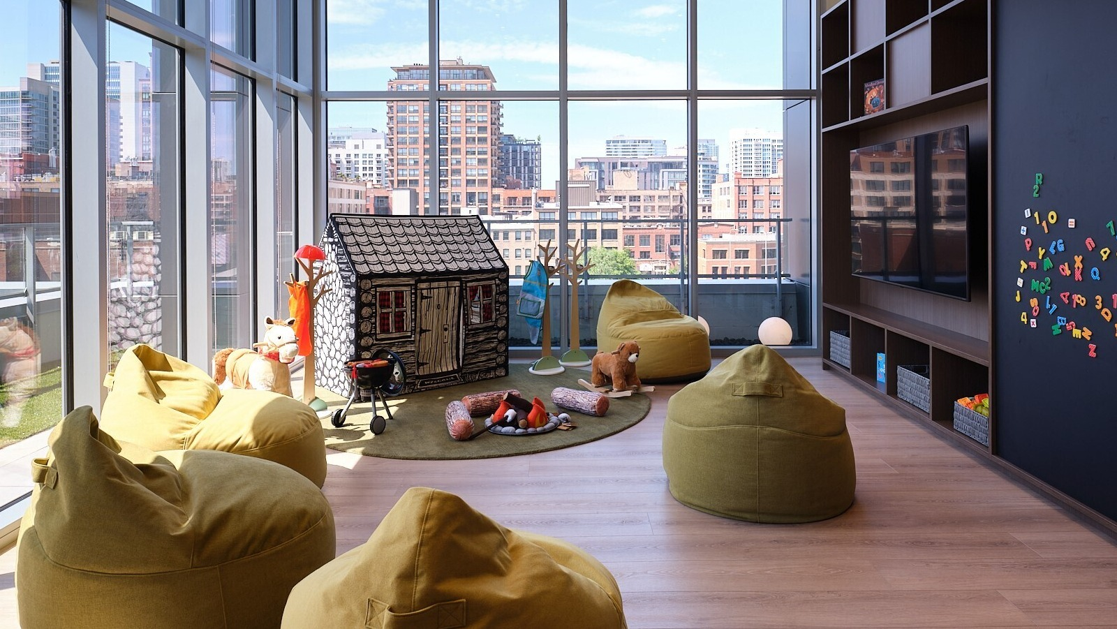 Children’s playroom with beanbag seating, playhouse, toys, and skyline views through tall windows at 369 Grand apartments in Chicago
