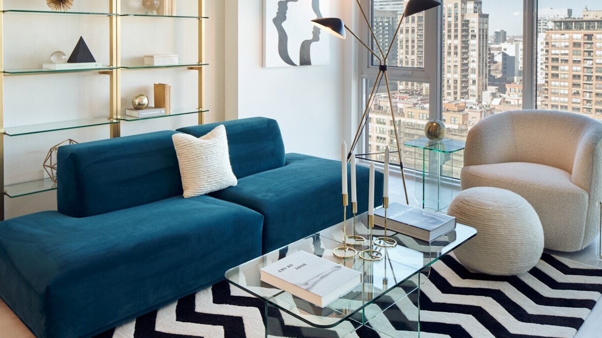 Cozy living room with teal sofa, chevron rug, glass coffee table, and floor-to-ceiling windows showcasing city views at 369 Grand apartments in Chicago